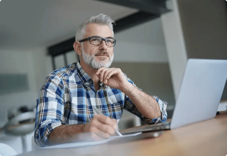 Man achter laptop kijkend naar buiten met bril