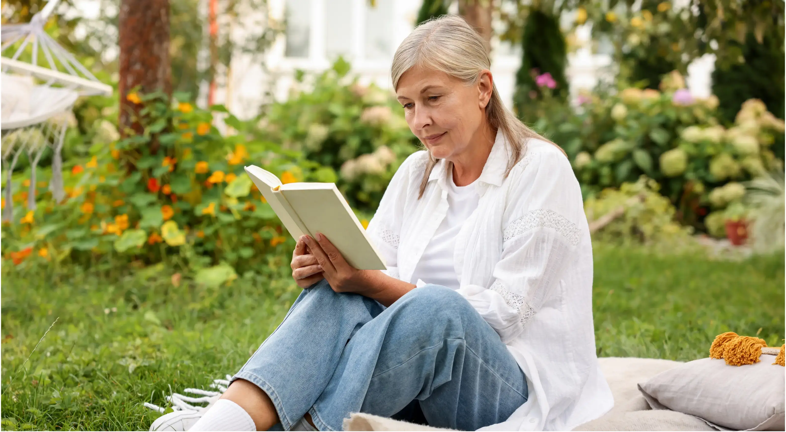 Oudere vrouw is eerder met pensioen en leest een boek in haar tuin.