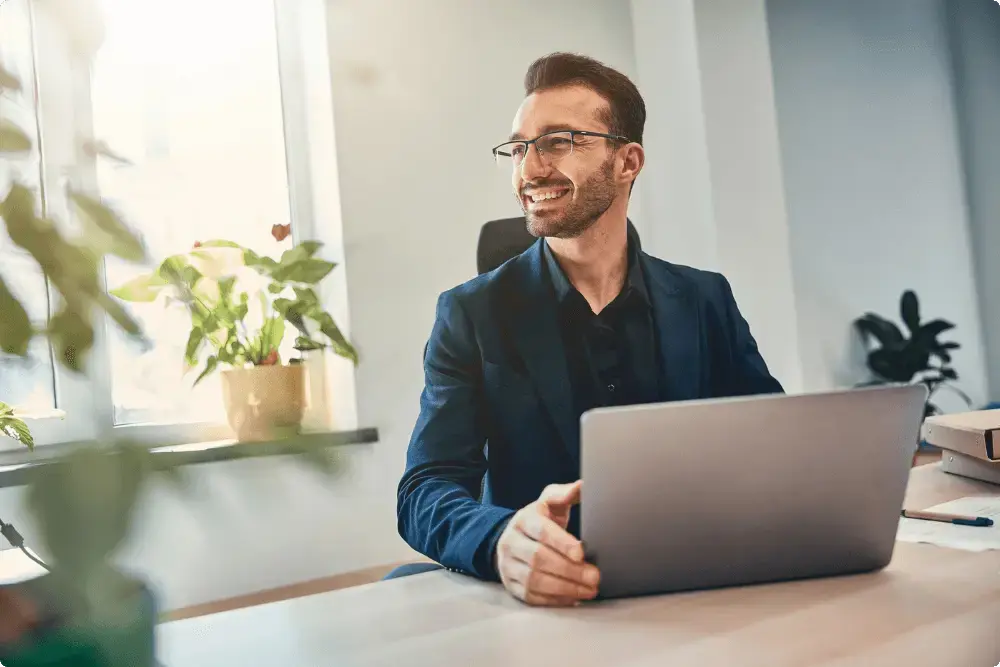 Man kijkt blij weg van zijn laptop omdat hij spreidt bij beleggen