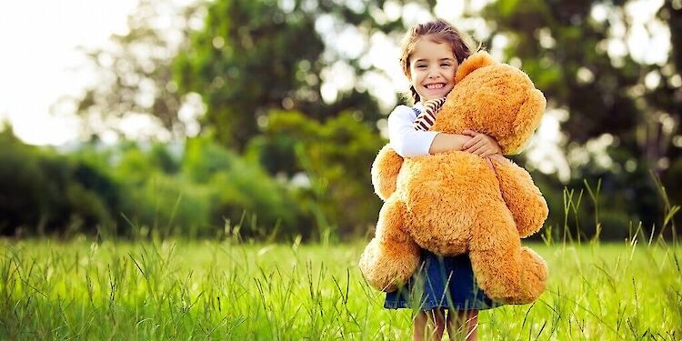 Meisje met grote teddybeer in armen die staat in gras
