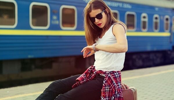 Vrouw die kijkt op horloge met een trein achter haar