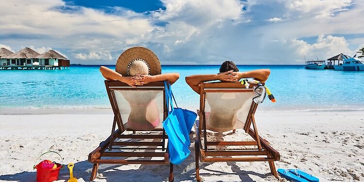 twee mensen die op een strandbedje liggen op het strand met blauw water