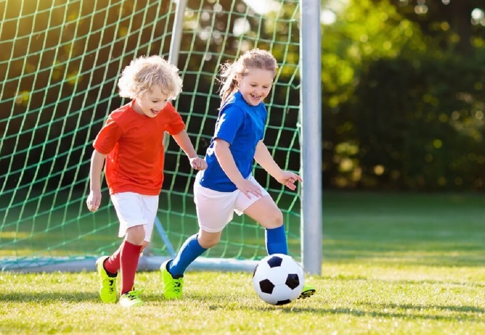 Jongen en meisje die voetballen in rood en blauw tenue.